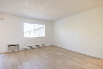 The living room of an apartment with wood flooring and a window